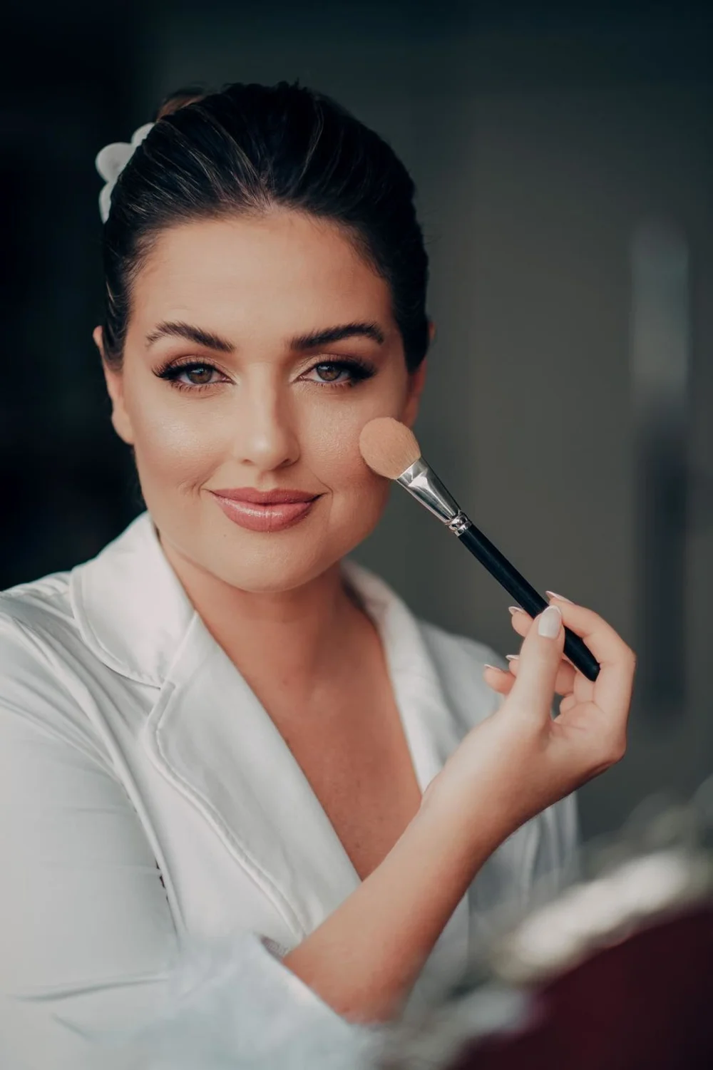 Noiva sorrindo enquanto recebe maquiagem com pincel profissional no dia do casamento